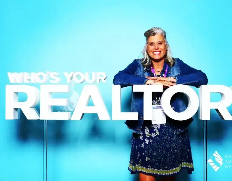 Cambria and San Simeon RE/MAX® real estate Broker Associate Jennifer Lawson standing with realtor sign.